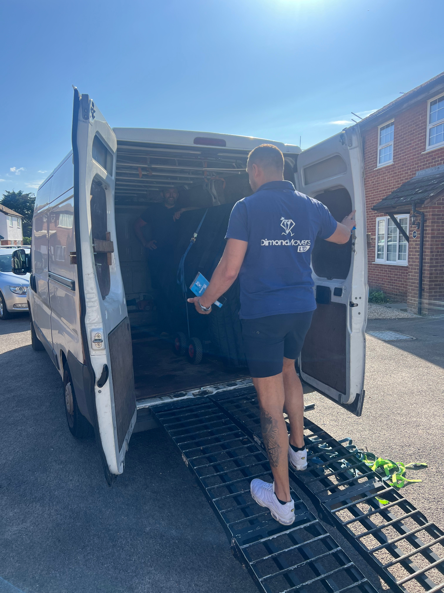 Dimond Movers crew loading a blanket-wrapped piano into the removals van using loading ramps outside a UK home