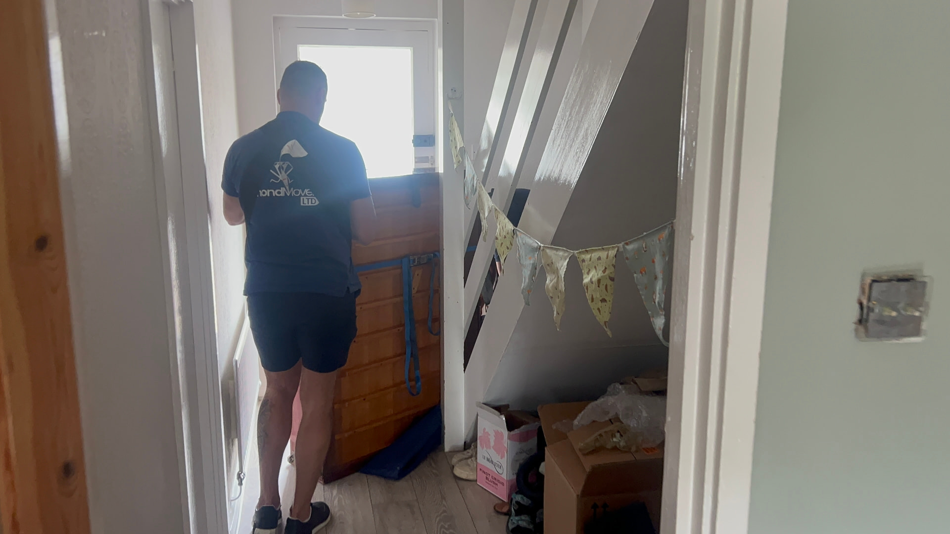 Dimond Movers crew member in branded uniform manoeuvring a strapped piano towards the front door