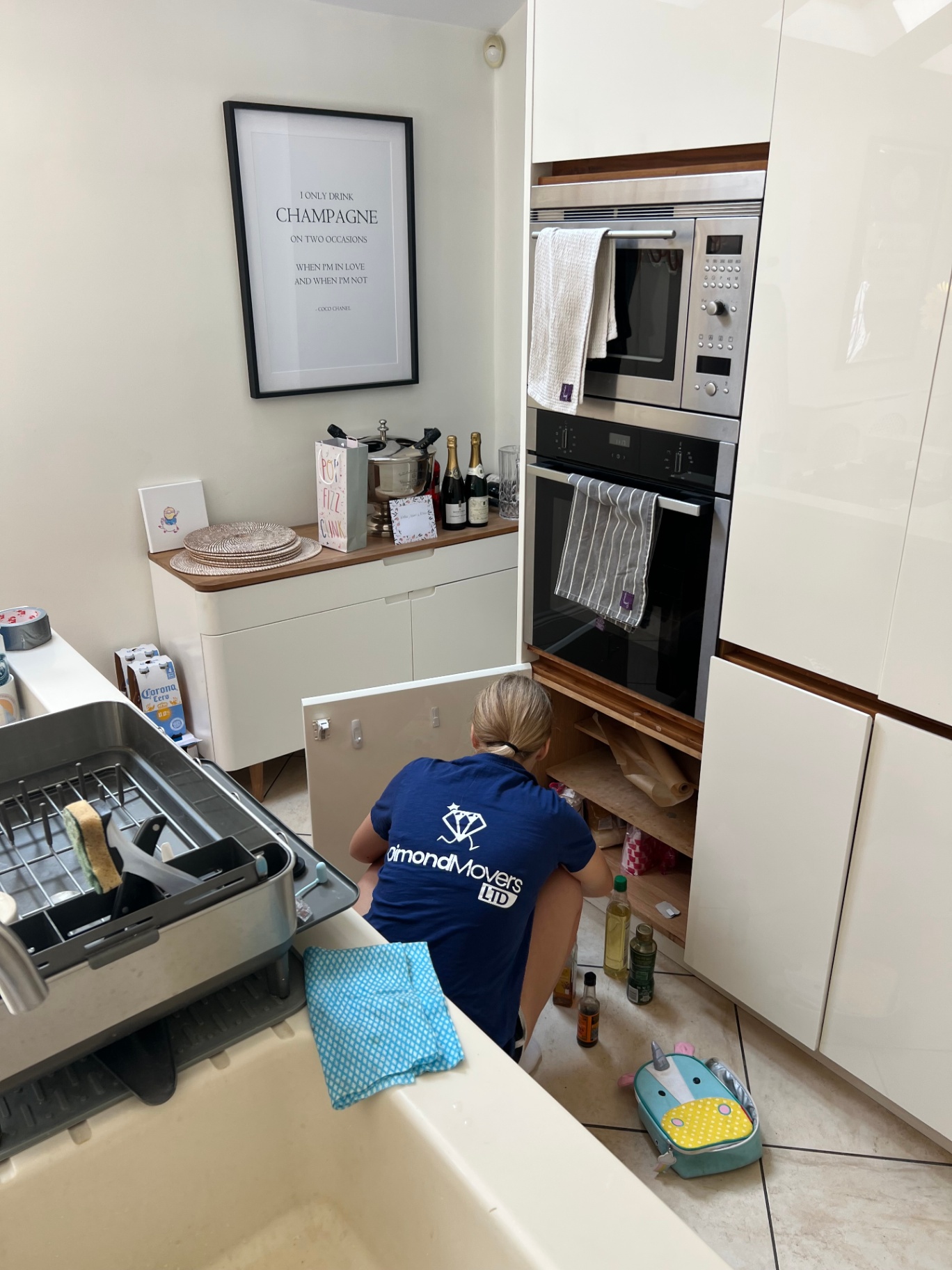 Dimond Movers packer packing bottles and kitchen items from a low cupboard