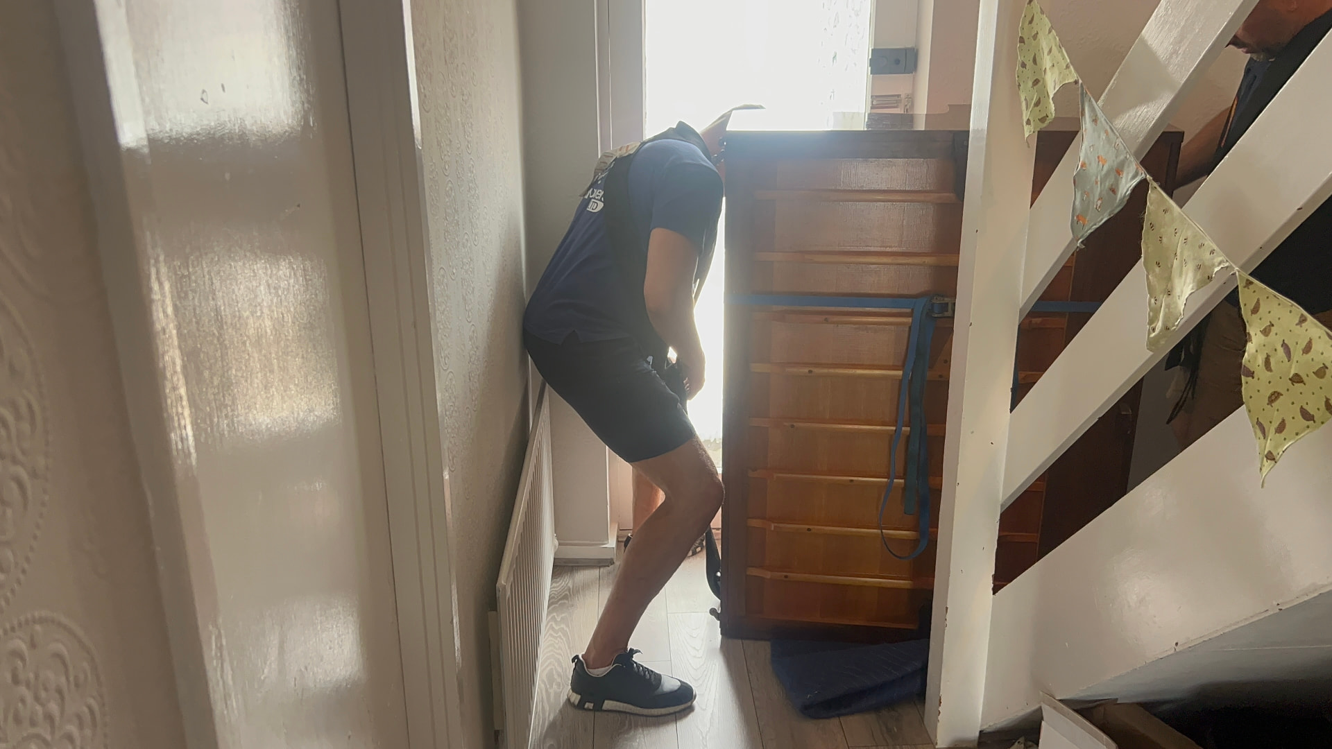 Dimond Movers mover guiding a strapped upright piano through a tight hallway beside a staircase