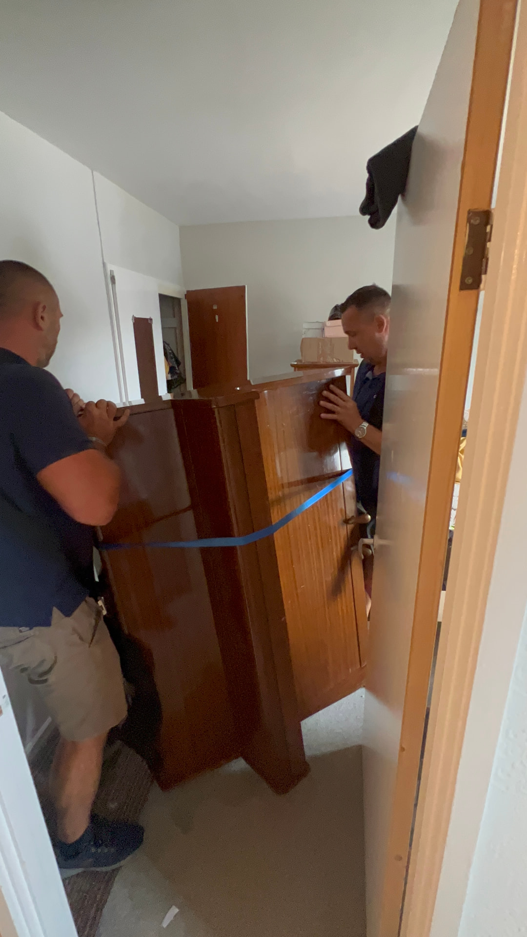 Two Dimond Movers movers carrying a strapped upright piano down a narrow staircase turn