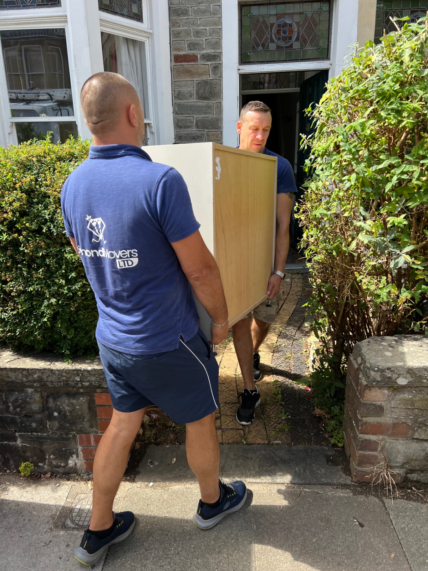 Dimond Movers team carrying a tall wardrobe through a Bristol stained glass front door