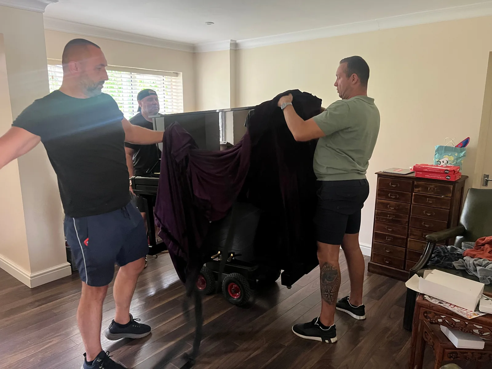 Dimond Movers crew wrapping an upright piano in premium moving blankets on a piano dolly inside a living room