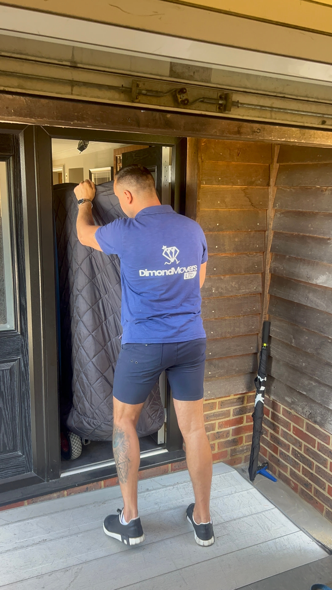 Dimond Movers specialist in branded uniform guiding a fully blanket-wrapped piano out through a front door