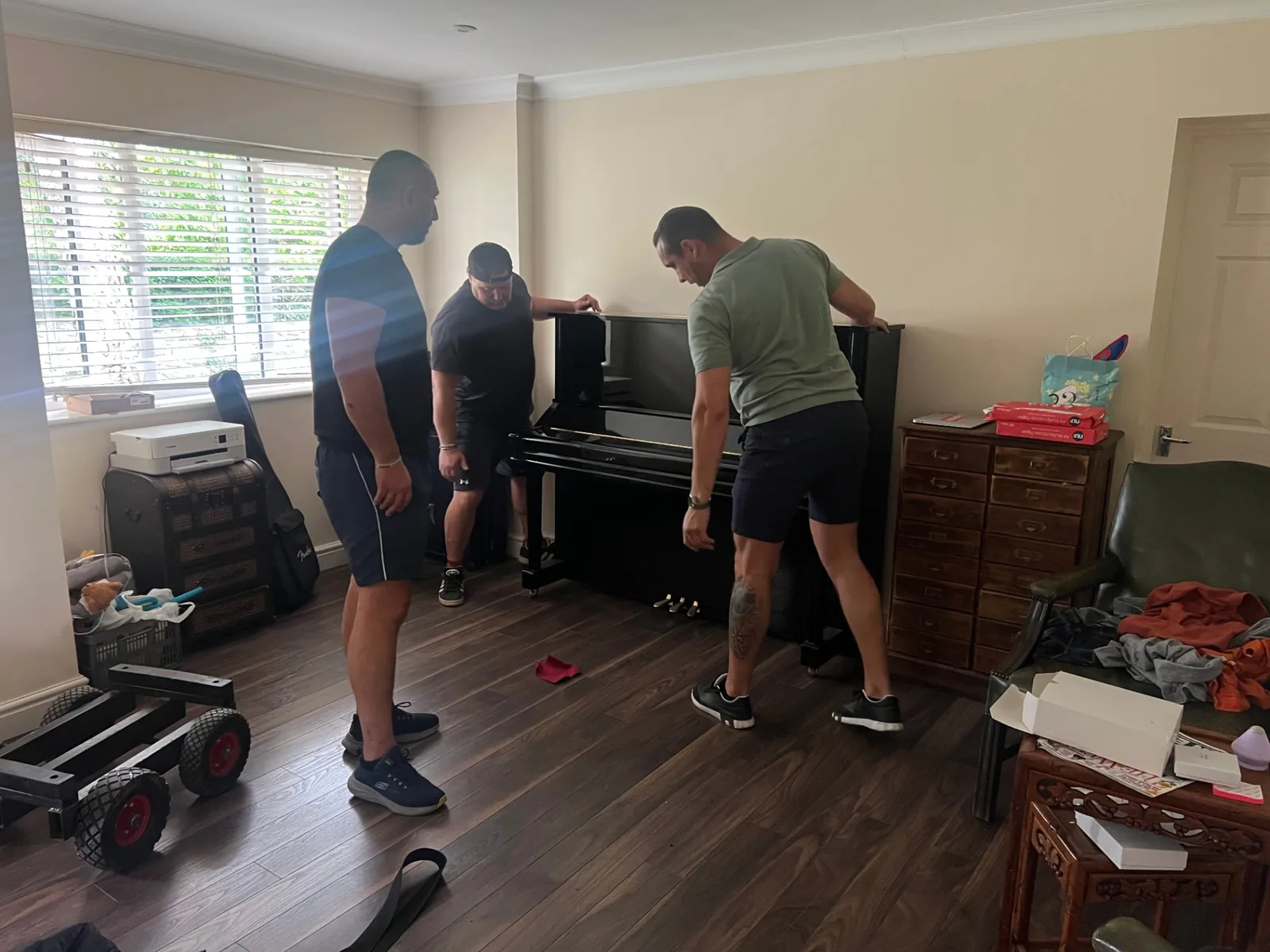 Dimond Movers piano team of three carefully lifting a black upright piano away from the wall in a family living room