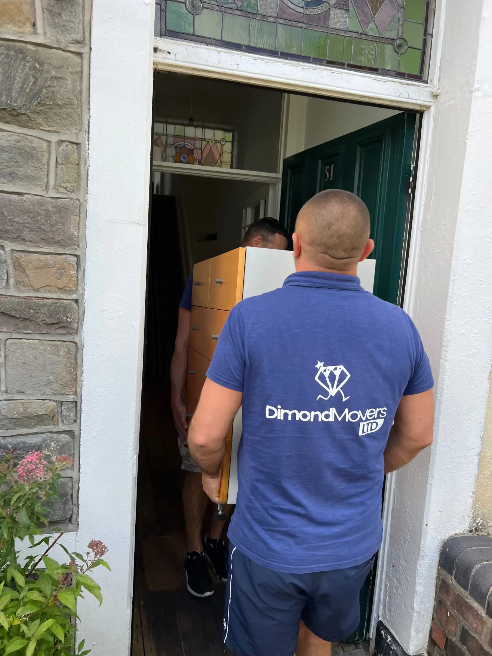 Dimond Movers team in branded uniform carrying a chest of drawers through a period property doorway