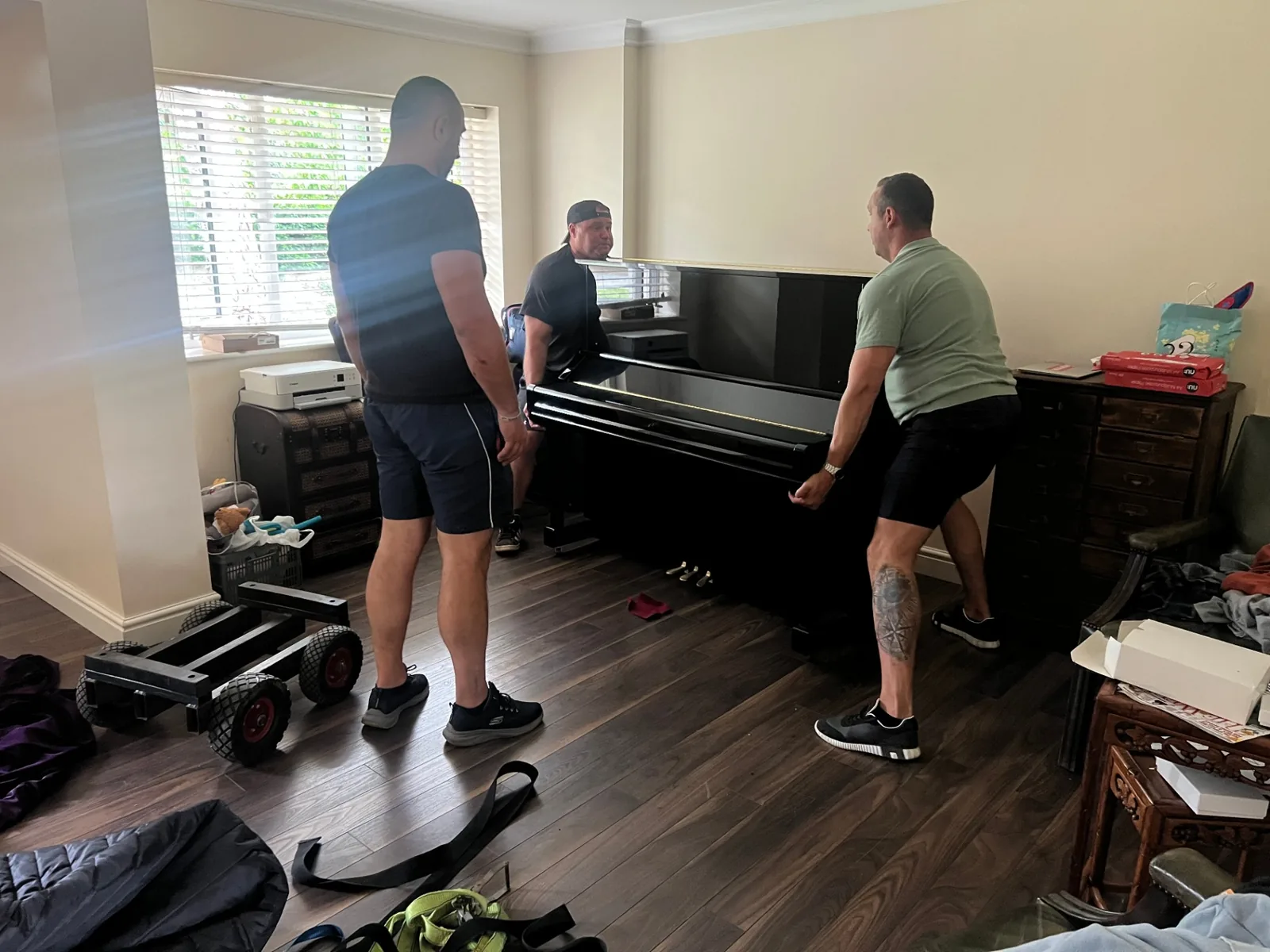 Dimond Movers movers repositioning a black upright piano onto a piano skid inside a home before wrapping