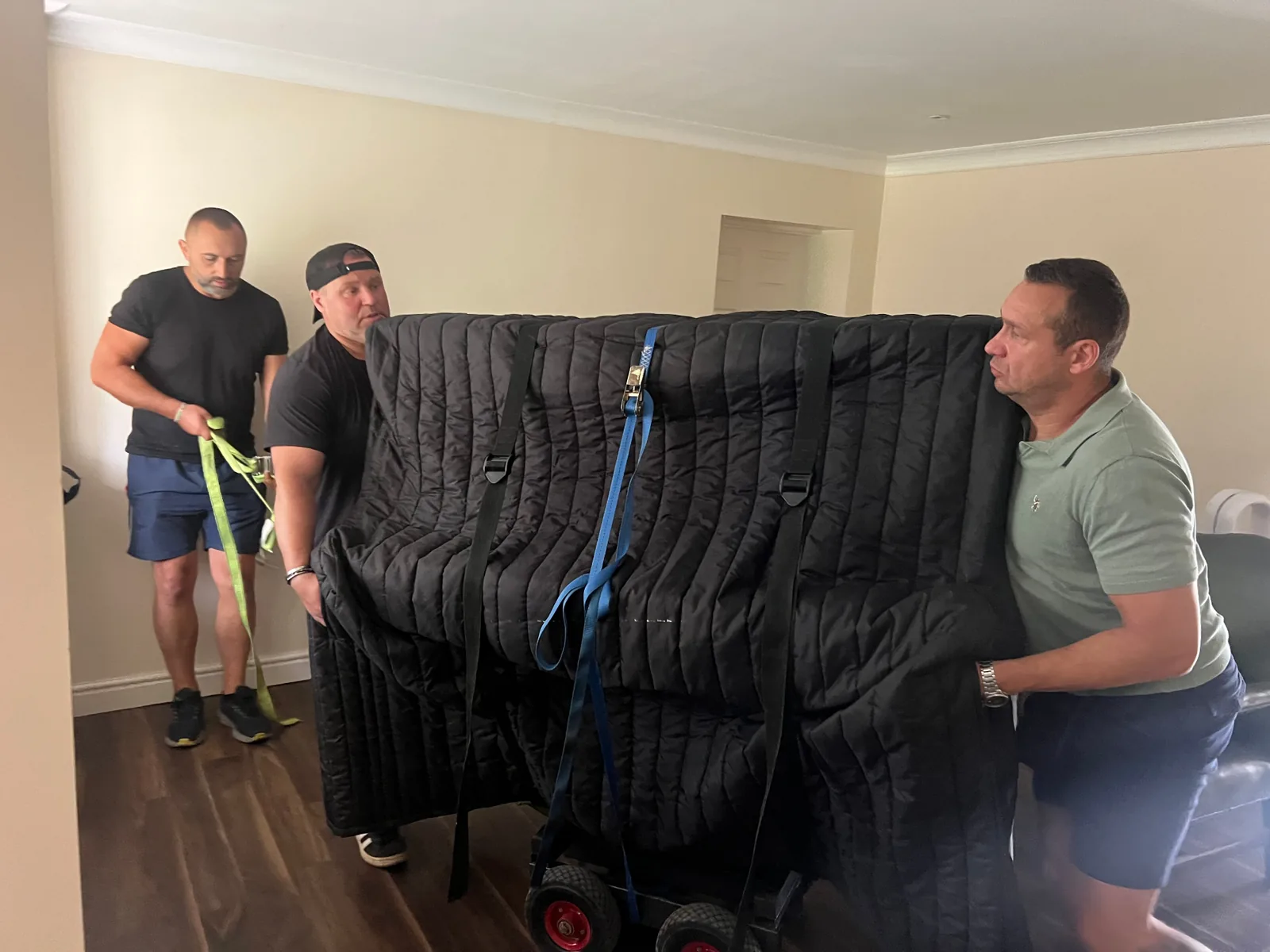 Fully blanket wrapped and ratchet strapped upright piano on a Dimond Movers piano dolly inside a UK home