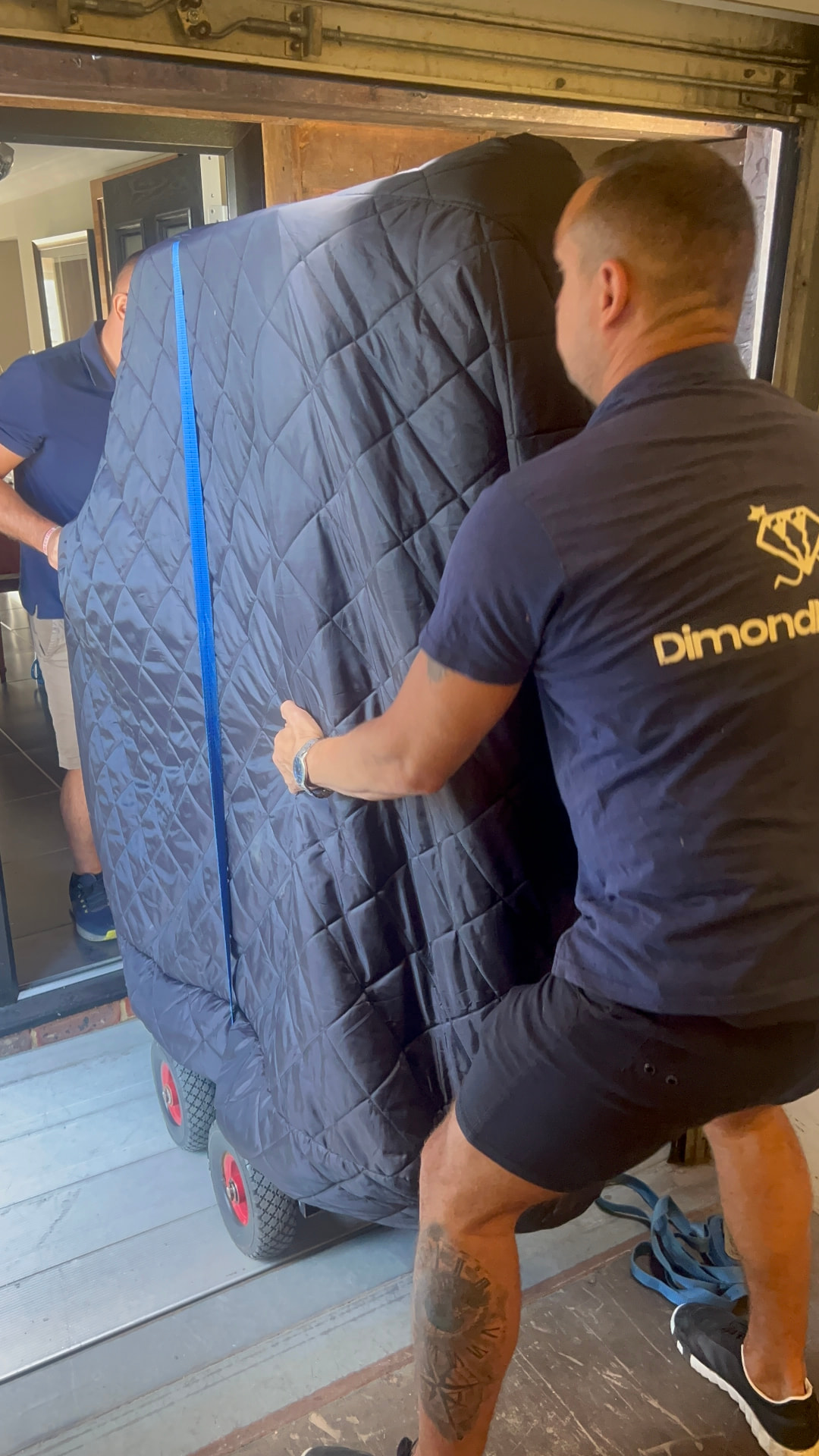 Two Dimond Movers movers wheeling a wrapped and strapped piano on a pneumatic-wheel piano dolly over a threshold