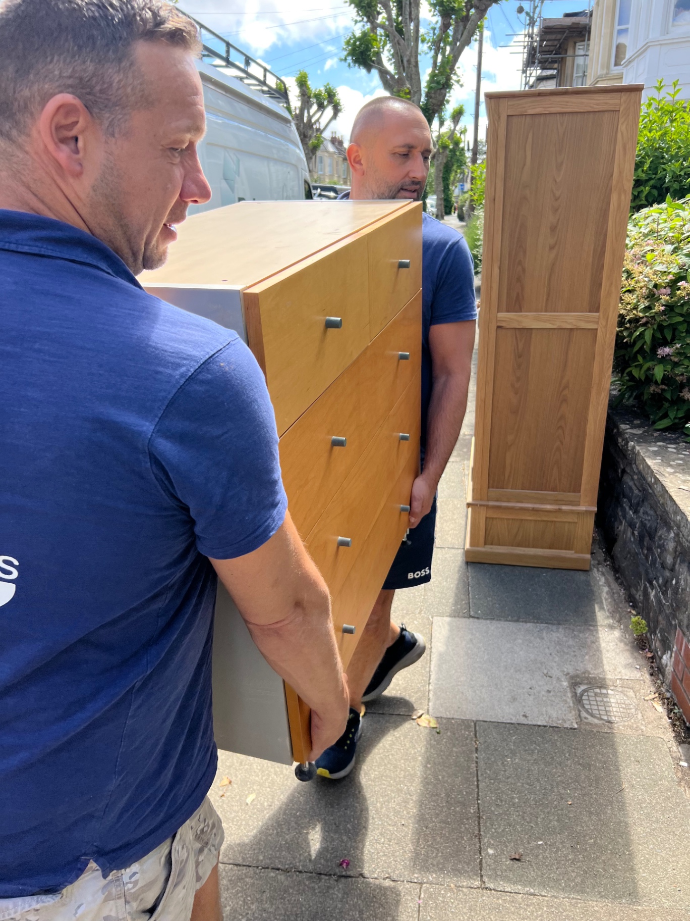 Two Dimond Movers carrying a heavy chest of drawers along a Bristol pavement during a real move